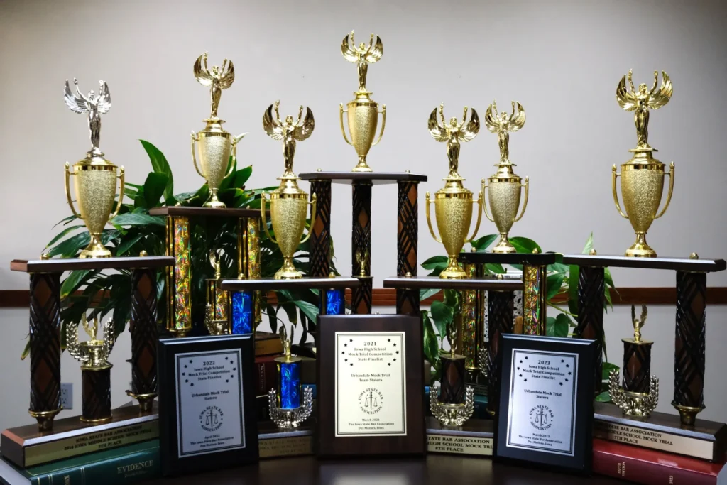 Collection of gold and silver mock trial competition trophies with plaques displayed on a table.