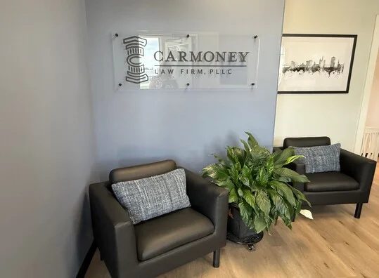 Reception area with two black armchairs, a large green plant, and Carmoney Law Firm sign.