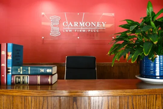 Reception desk with legal books, black chair, green potted plant, and Carmoney Law Firm sign.