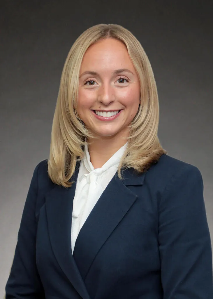 Professional portrait of a smiling woman with blonde hair wearing a navy blazer and white blouse.